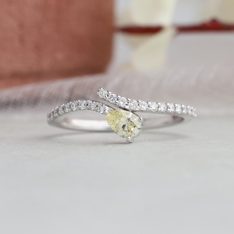 Peut inclure: Une bague bypass argent&eacute;e orn&eacute;e d'une pierre centrale jaune p&acirc;le en forme de poire et d'un anneau agr&eacute;ment&eacute; de petites pierres claires. L'anneau m&eacute;tallique se courbe autour de la pierre centrale, cr&eacute;ant un aspect superpos&eacute; et &eacute;l&eacute;gant.