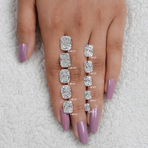 K&ouml;nnte beinhalten: Ein Handmodell mit helllila lackierten N&auml;geln zeigt einen Gr&ouml;&szlig;envergleich von Kissen-Schliff-Diamanten. Die Diamanten reichen von 0,50 Karat bis 5,00 Karat. Jeder Diamant ist mit seinem Karatgewicht gekennzeichnet.