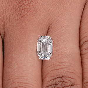 May include: A clear emerald cut diamond gemstone on a finger.