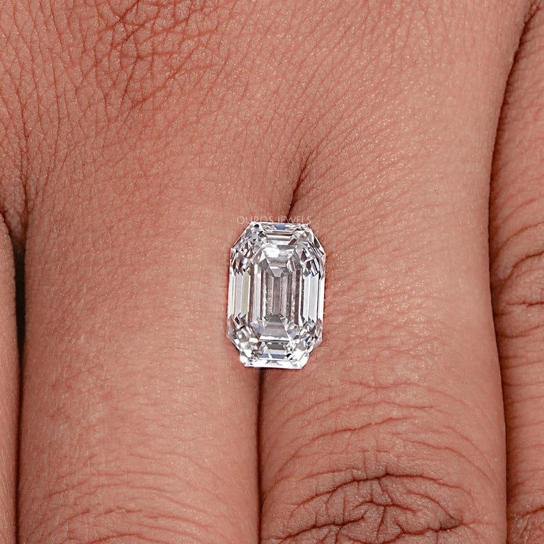 May include: A clear emerald cut diamond gemstone on a finger.