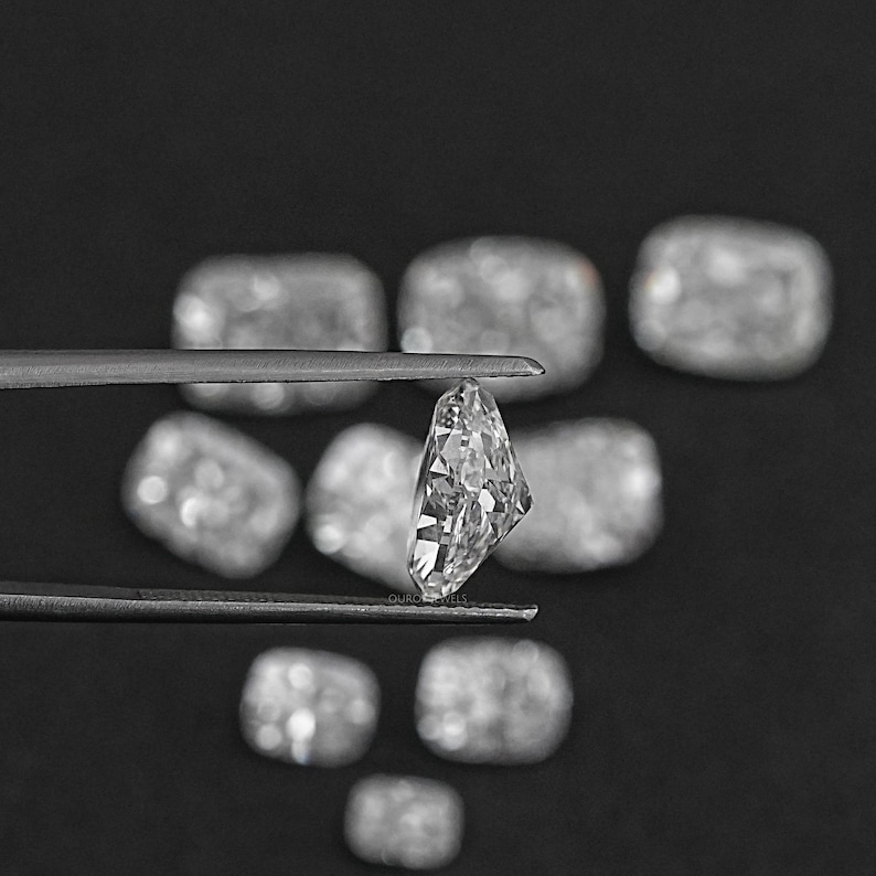 K&ouml;nnte beinhalten: Ein klarer, facettierter, rechteckiger Diamant-Edelstein, der mit einer Pinzette gehalten wird. Der Diamant ist von anderen &auml;hnlichen Edelsteinen auf schwarzem Hintergrund umgeben.
