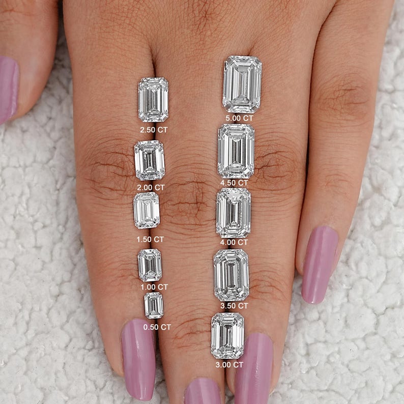 May include: A hand model wearing a clear nail polish displays a size comparison of ten emerald cut diamonds. The diamonds are arranged in a row from smallest to largest, with the carat weight of each diamond labeled below it. The diamonds range in size from 0.50 carats to 5.00 carats.