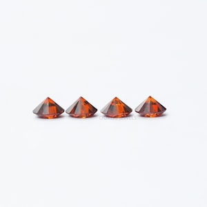 Puede incluir: Cuatro piedras preciosas redondas, facetadas, de color naranja. Las piedras preciosas est&aacute;n dispuestas en una fila sobre una superficie blanca.