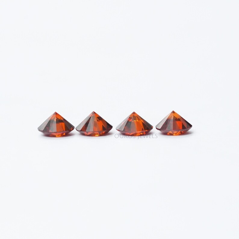 Puede incluir: Cuatro piedras preciosas redondas, facetadas, de color naranja. Las piedras preciosas est&aacute;n dispuestas en una fila sobre una superficie blanca.