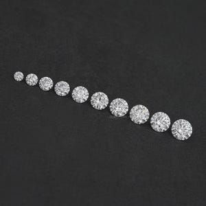 May include: A row of round, clear, faceted gemstones of varying sizes, arranged from smallest to largest on a black surface.