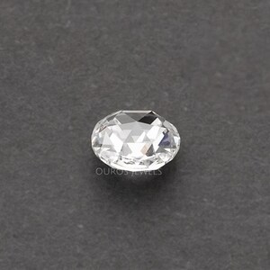 K&ouml;nnte beinhalten: Ein klarer, facettierter, ovaler Edelstein mit Rosenschliff, der mehrere dreieckige Facetten aufweist, die das Licht reflektieren. Der Text OUROS JEWELS ist in kleinen, hellen Buchstaben direkt unter dem Edelstein aufgedruckt.