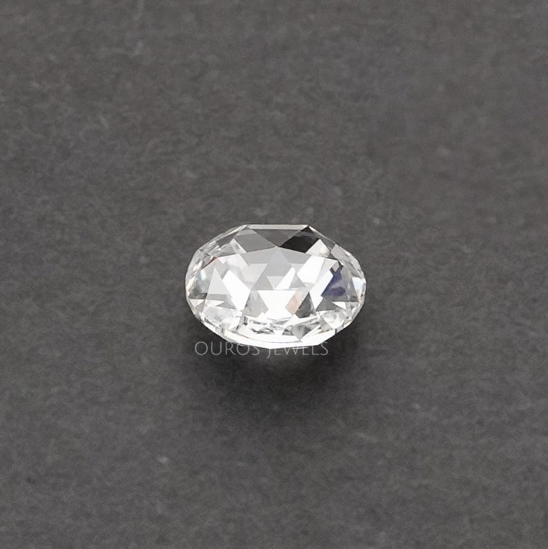K&ouml;nnte beinhalten: Ein klarer, facettierter, ovaler Edelstein mit Rosenschliff, der mehrere dreieckige Facetten aufweist, die das Licht reflektieren. Der Text OUROS JEWELS ist in kleinen, hellen Buchstaben direkt unter dem Edelstein aufgedruckt.