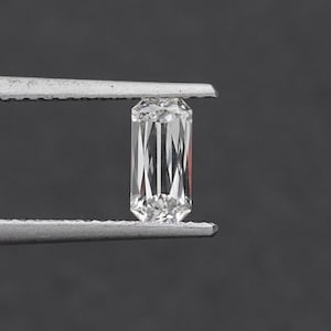 May include: A clear, rectangular emerald cut diamond gemstone held by tweezers.