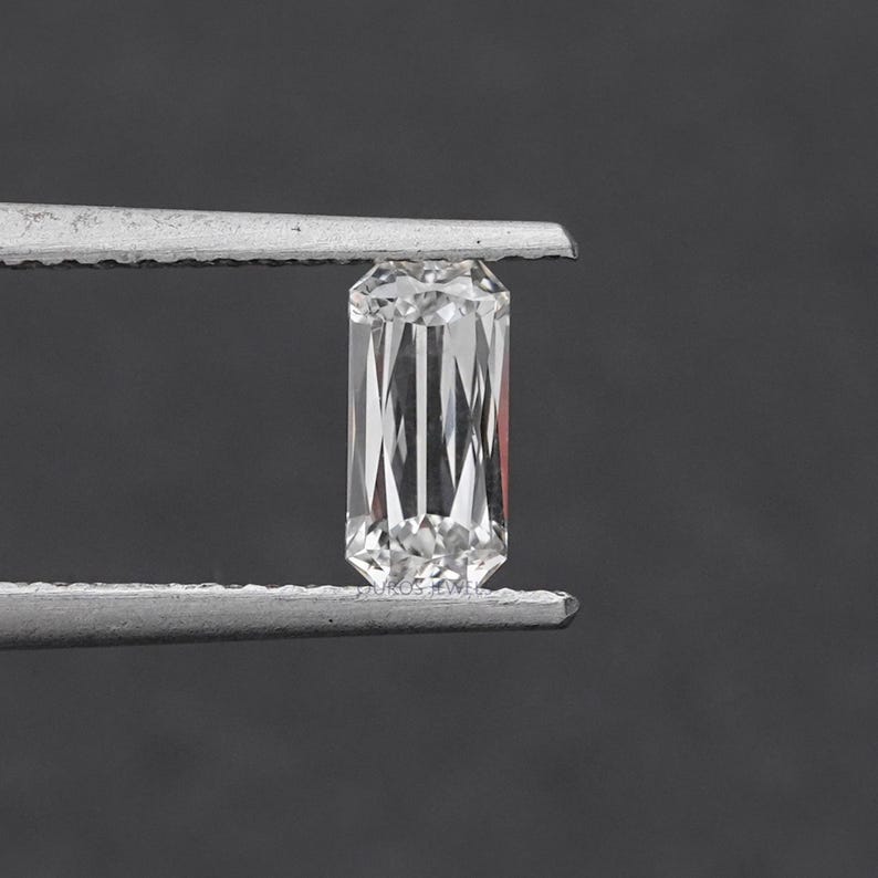 May include: A clear, rectangular emerald cut diamond gemstone held by tweezers.
