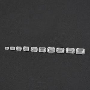 May include: A set of 11 emerald cut diamonds of varying sizes, arranged in a row on a black surface.