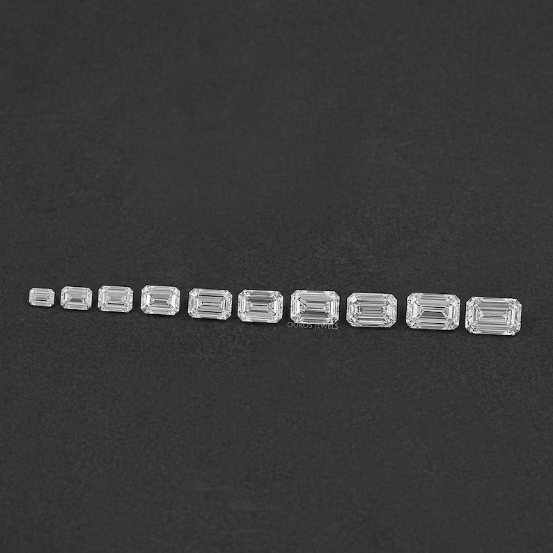 May include: A set of 11 emerald cut diamonds of varying sizes, arranged in a row on a black surface.