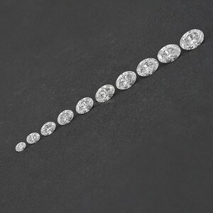 Pu&ograve; includere: Una fila di diamanti di forma ovale di diverse dimensioni, disposti in ordine crescente dal pi&ugrave; piccolo al pi&ugrave; grande, su uno sfondo nero.