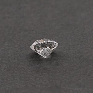 May include: A clear, round, faceted gemstone with a brilliant cut. The gemstone is set against a dark gray background.