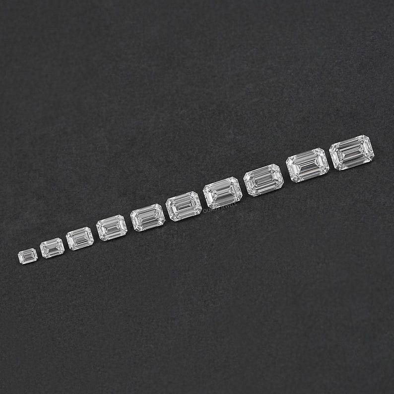 May include: A row of ten clear emerald cut diamonds of varying sizes, arranged in ascending order from left to right on a black surface.