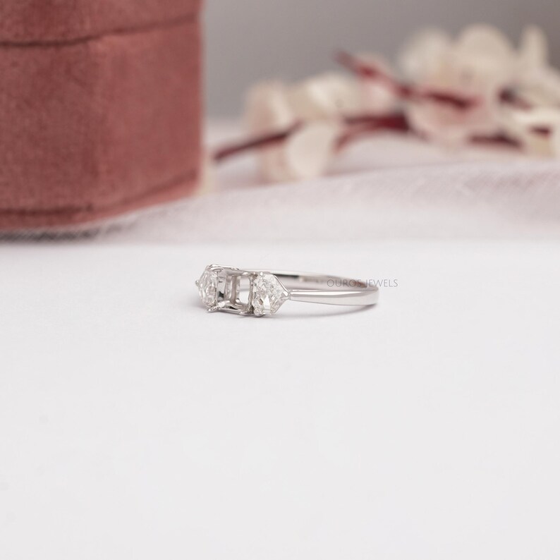 May include: A silver-toned metal ring featuring a central rectangular setting flanked by two smaller, triangular-shaped clear stones on each side. The band is smooth and polished, showcasing a three-stone design with a minimalist, clean aesthetic.