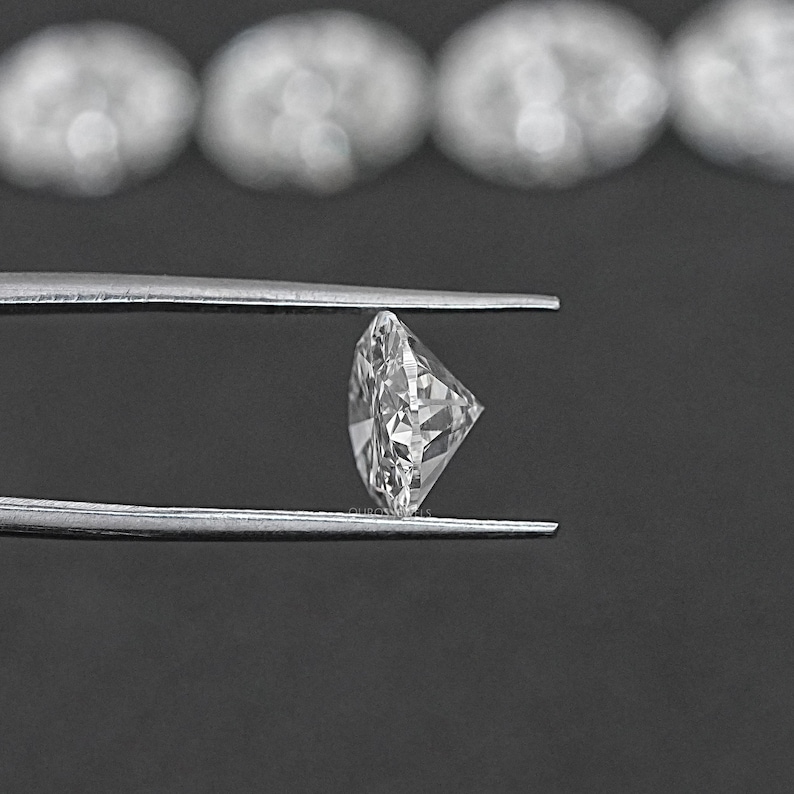 Pu&ograve; includere: Un diamante rotondo e trasparente tenuto in una pinza su uno sfondo nero.