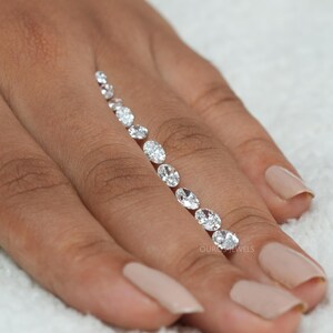 May include: A line of oval-shaped diamonds of varying sizes, arranged in a row on a person's finger. The diamonds are clear and sparkly, and they are set in a simple, elegant style.