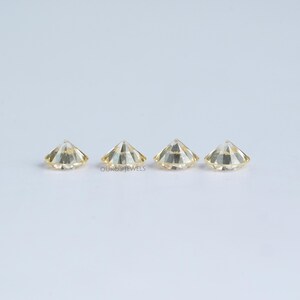 May include: Three round, faceted, light yellow gemstones, set in a row on a white surface.