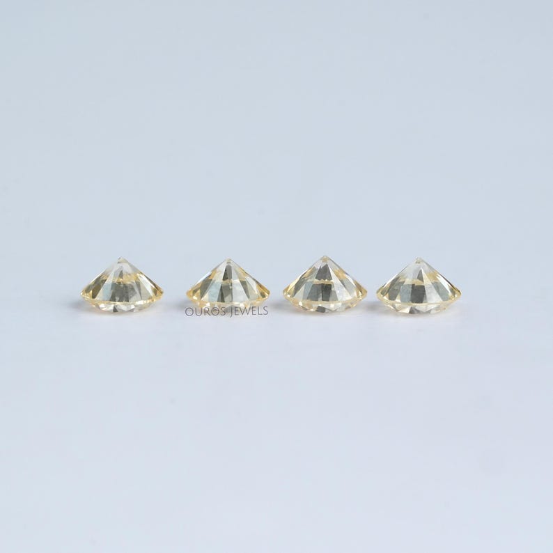 May include: Three round, faceted, light yellow gemstones, set in a row on a white surface.