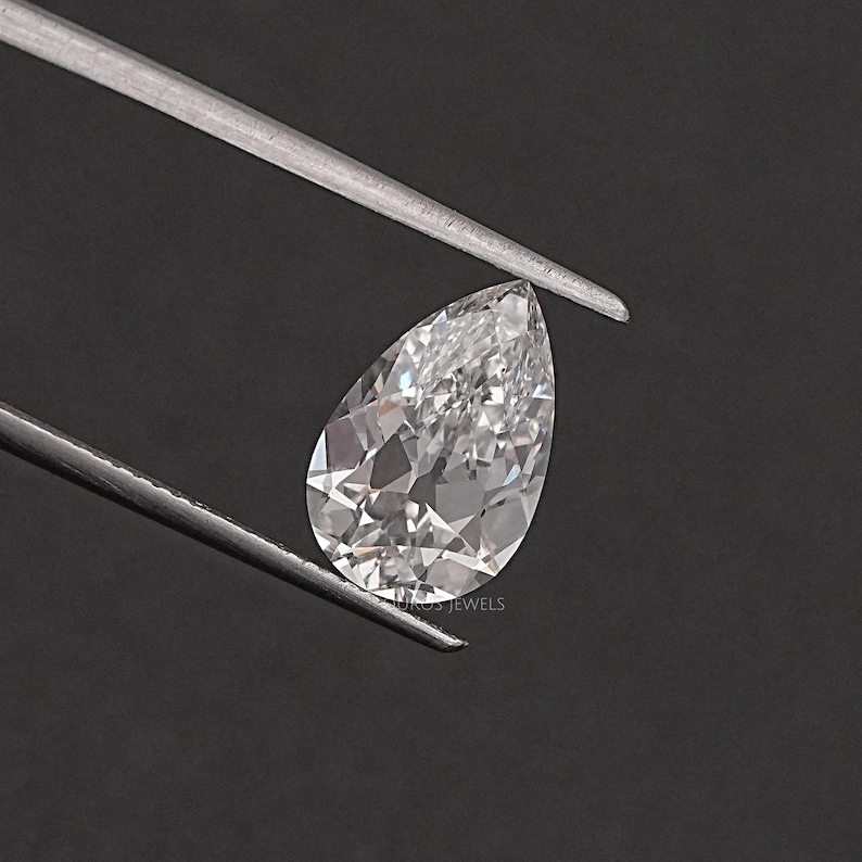 May include: A pear-shaped, clear gemstone with a slight pink hue. The gemstone is held by tweezers against a black background.