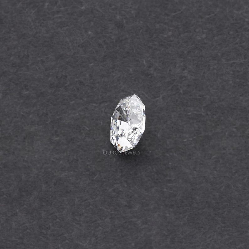 May include: A clear, faceted diamond with a marquise cut, set against a dark gray background. The diamond's multiple facets reflect light, creating a sparkling effect. The word "OURO JEWELS" is visible at the bottom.