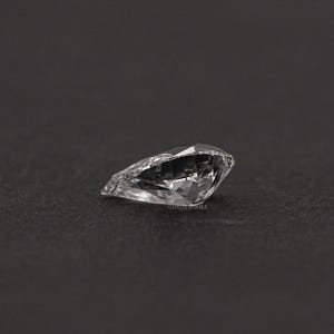May include: A clear, pear-shaped gemstone with many facets. The gemstone is set against a black background.