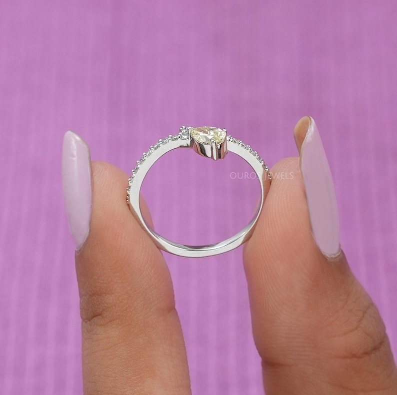 Peut inclure: Une bague argent&eacute;e orn&eacute;e d'une pierre pr&eacute;cieuse jaune clair en forme de poire au centre, entour&eacute;e d'un anneau incrust&eacute; de petites pierres transparentes. L'anneau en m&eacute;tal est poli et brillant, avec le texte OURO JEWELS visible &agrave; l'int&eacute;rieur.