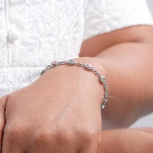 Puede incluir: Un brazalete de plata con una cadena delicada y peque&ntilde;as piedras preciosas de colores. El brazalete presenta un patr&oacute;n repetitivo de piedras ovaladas engastadas en un halo de piedras m&aacute;s peque&ntilde;as.