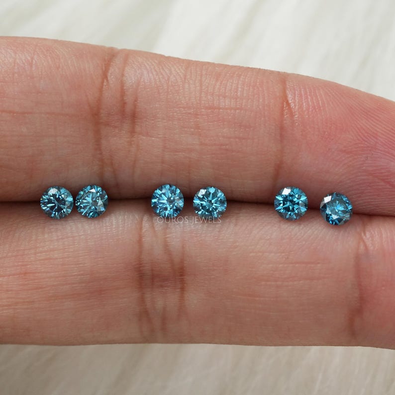 May include: Six round, blue gemstones are arranged in a row on a finger. The gemstones are all the same size and shape.