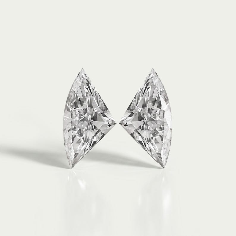 Puede incluir: Dos piedras preciosas incoloras de corte triangular con esquinas afiladas y m&uacute;ltiples facetas triangulares. Las piedras est&aacute;n colocadas una al lado de la otra, reflejando la luz con gran brillo y claridad, mostrando una apariencia clara y transparente.
