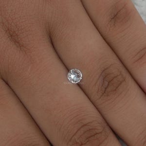 K&ouml;nnte beinhalten: Ein kleiner, runder, im Brillantschliff gehaltener loser Diamant mit klarem, farblosem Aussehen und zahlreichen Facetten, die das Licht reflektieren. Der Edelstein ist mittig platziert und zeigt eine kreisf&ouml;rmige Form sowie eine polierte Oberfl&auml;che.