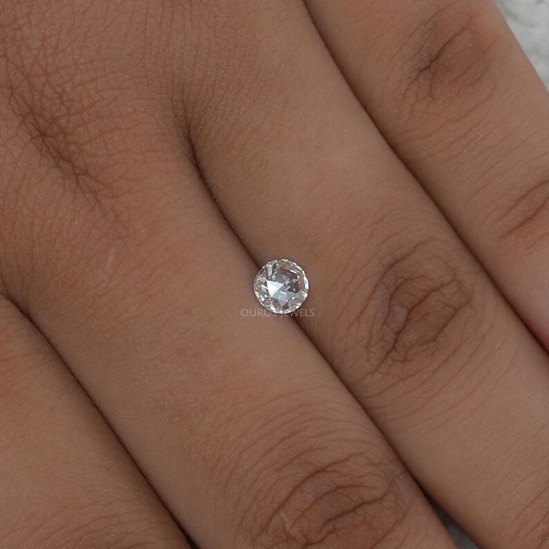 K&ouml;nnte beinhalten: Ein kleiner, runder, im Brillantschliff gehaltener loser Diamant mit klarem, farblosem Aussehen und zahlreichen Facetten, die das Licht reflektieren. Der Edelstein ist mittig platziert und zeigt eine kreisf&ouml;rmige Form sowie eine polierte Oberfl&auml;che.