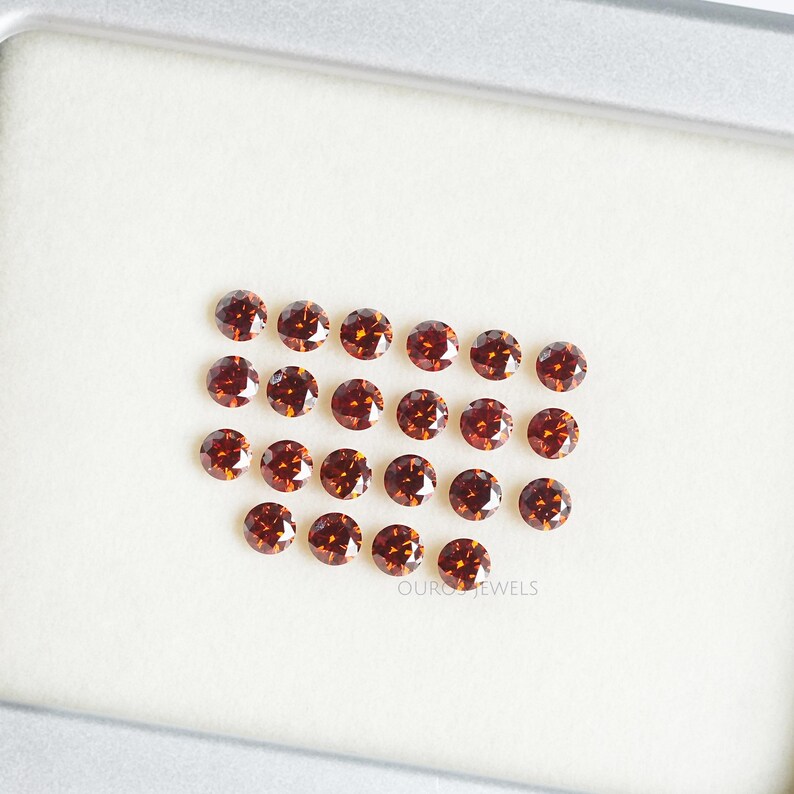 Puede incluir: Una colecci&oacute;n de 20 diamantes redondos de color marr&oacute;n dispuestos en forma de coraz&oacute;n sobre una superficie blanca. Los diamantes son todos del mismo tama&ntilde;o y tienen un corte brillante.