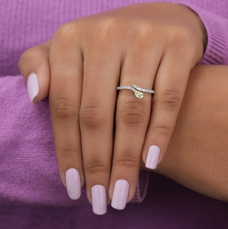 Peut inclure: Une bague bypass argent&eacute;e avec une pierre centrale jaune en forme de poire et un anneau orn&eacute; de petites pierres claires. La bague pr&eacute;sente un design d&eacute;licat et ouvert qui s'enroule autour du doigt, mettant en valeur une pierre jaune facett&eacute;e.