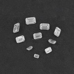 May include: Assortment of emerald cut diamonds of various sizes on a black background.