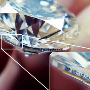 May include: Close-up of a clear diamond with a silver band. The diamond has a laser inscription that reads "639 M1D12345".