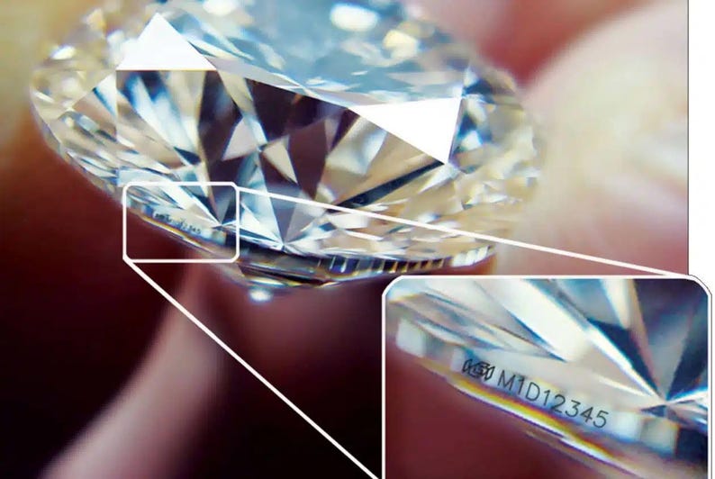 May include: Close-up of a clear diamond with a silver band. The diamond has a laser inscription that reads "639 M1D12345".