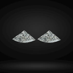 Puede incluir: Dos diamantes incoloros sueltos de talla trillion con bordes facetados afilados y gran brillo. Cada piedra preciosa muestra una forma triangular con lados curvos que reflejan la luz. El texto OUROS JEWELS es visible.