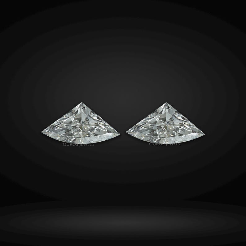 Puede incluir: Dos diamantes incoloros sueltos de talla trillion con bordes facetados afilados y gran brillo. Cada piedra preciosa muestra una forma triangular con lados curvos que reflejan la luz. El texto OUROS JEWELS es visible.