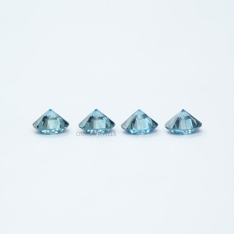 May include: Three round, faceted, light blue gemstones. The gemstones are arranged in a row on a white surface.