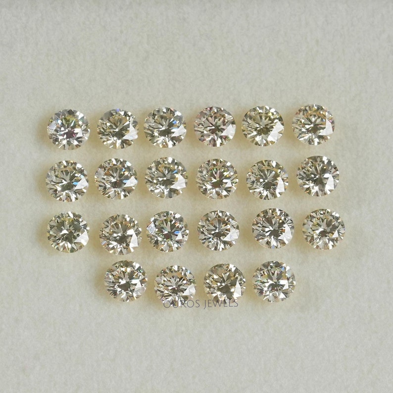 May include: A collection of 19 round, clear, faceted, loose diamonds in various sizes. The diamonds are arranged in rows on a white surface.