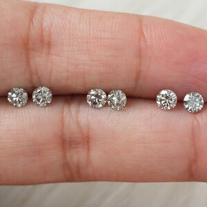 May include: Six round, clear, faceted gemstones on a finger. The gemstones are arranged in two rows of three. The gemstones are likely diamonds.