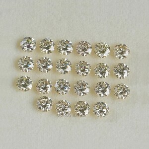 May include: A collection of 20 round, clear, faceted, loose diamonds. The diamonds are arranged in rows on a white surface.