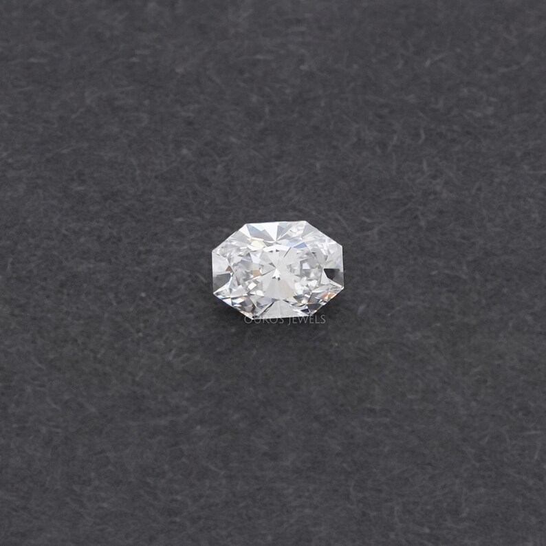 May include: A radiant-cut diamond with a brilliant, multifaceted surface. The gemstone is set against a dark gray background. The diamond's facets reflect light, creating a sparkling effect. The image is a close-up, highlighting the clarity and brilliance of the gem.
