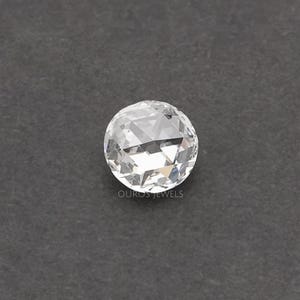 K&ouml;nnte beinhalten: Ein runder, facettierter, farbloser Edelstein im Rosenschliff mit flacher Basis und gew&ouml;lbter, mehrfach facettierter Oberseite, die Licht reflektiert. Der Text OUROS JEWELS ist in kleinen, wei&szlig;en Gro&szlig;buchstaben unter dem Stein gedruckt.