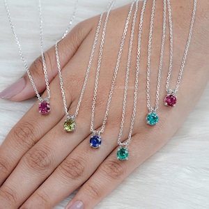 May include: Five silver necklaces with different colored gemstone pendants. The pendants are round and have a bezel setting. The colors of the gemstones are red, green, blue, and two shades of green.