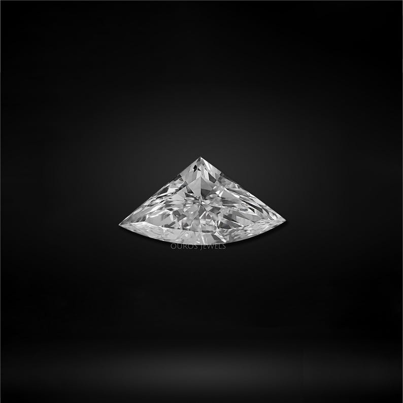 Puede incluir: Un diamante incoloro suelto con corte de escudo y superficie de facetas brillantes, que muestra bordes geom&eacute;tricos afilados y una punta superior. La piedra preciosa tiene el texto OUROS JEWELS en letras blancas en el centro.