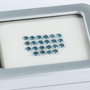 May include: A collection of 25 round, blue gemstones in a white, rectangular box. The gemstones are arranged in a grid pattern.