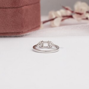 May include: A silver-toned metal ring setting featuring a central rectangular prong mount flanked by two smaller side stone settings. The band is smooth and polished, designed to hold a main gemstone and two accent stones in a three-stone arrangement.