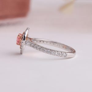 May include: A silver-toned ring featuring a central peach-colored gemstone surrounded by a halo of small white stones. The band is also encrusted with a row of small white stones along the sides, extending from the central setting.